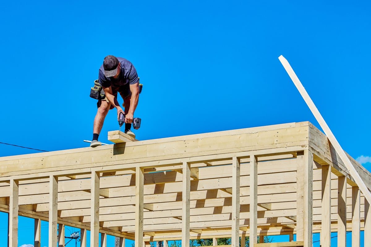Timber frame assembly as a worker installs lumber at roof level with a power tool