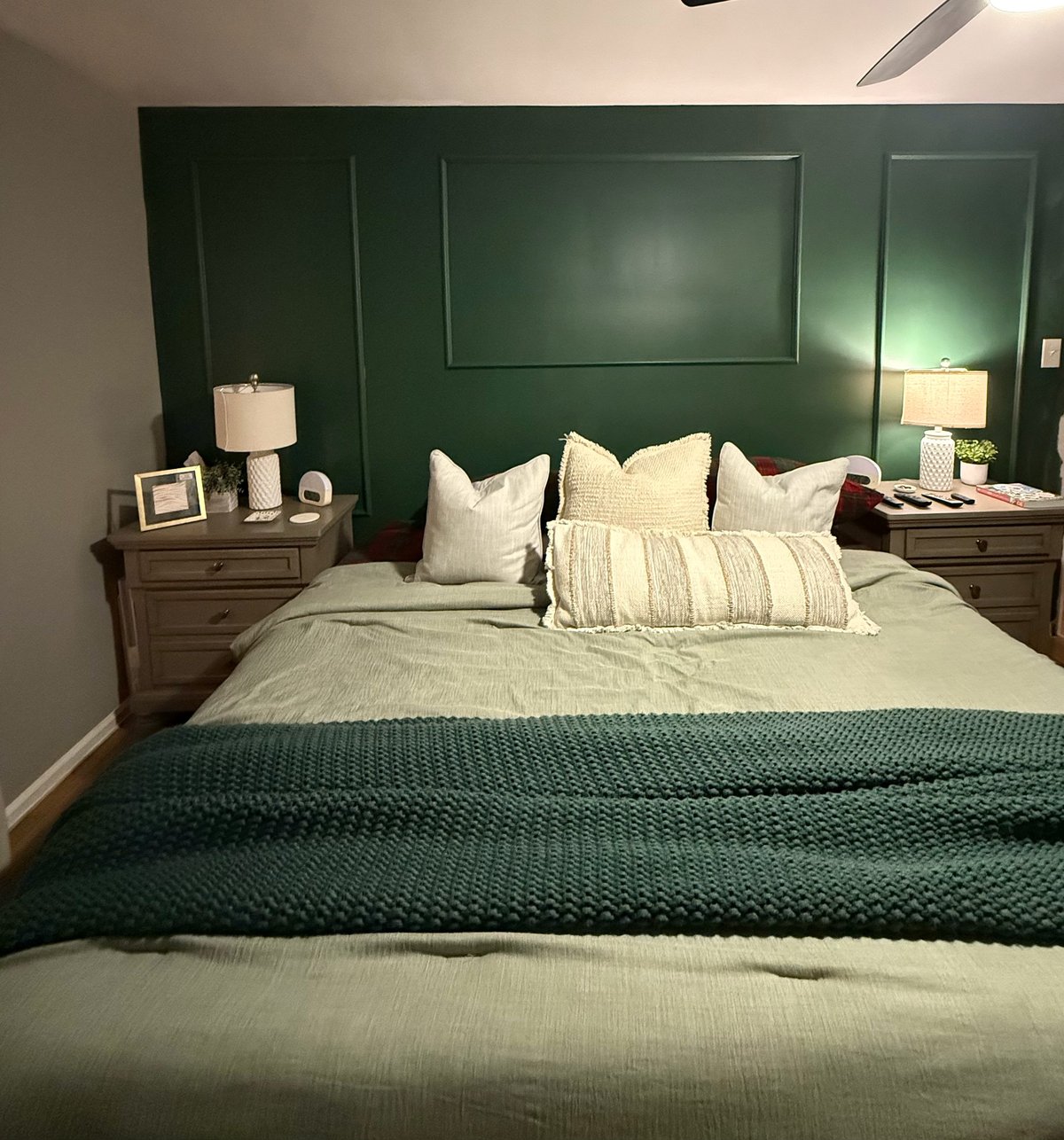 Modern bedroom with dark green accent wall, cream and white bedding, dark wood nightstands, and table lamps on either side