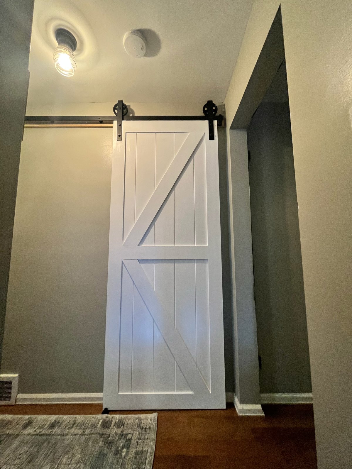 White barn door on black sliding track mounted in modern hallway with recessed lighting